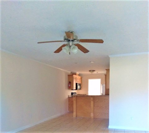 an empty living room with a ceiling fan and a kitchen