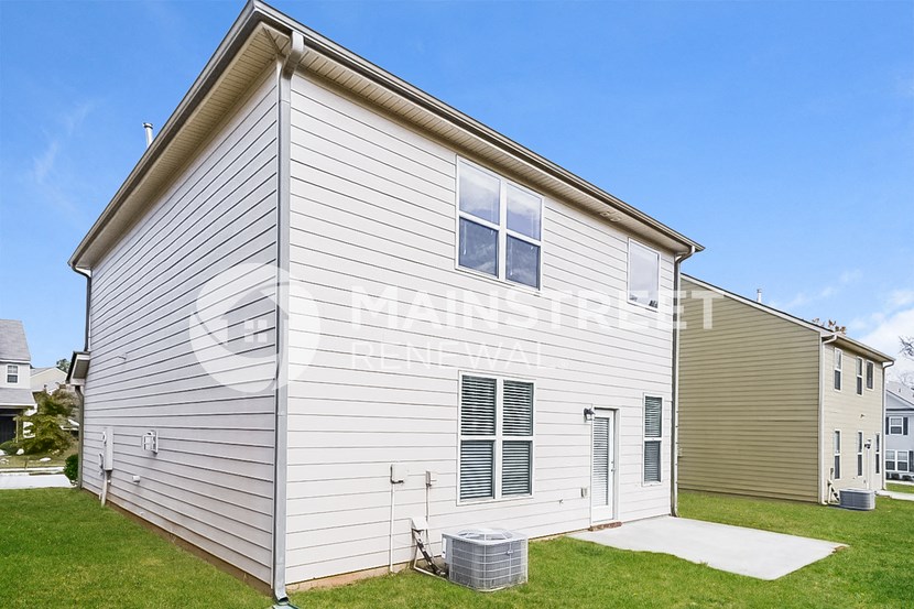 the outside of a white house with tan siding and green grass