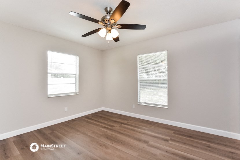 the spacious living room with a ceiling fan and two windows