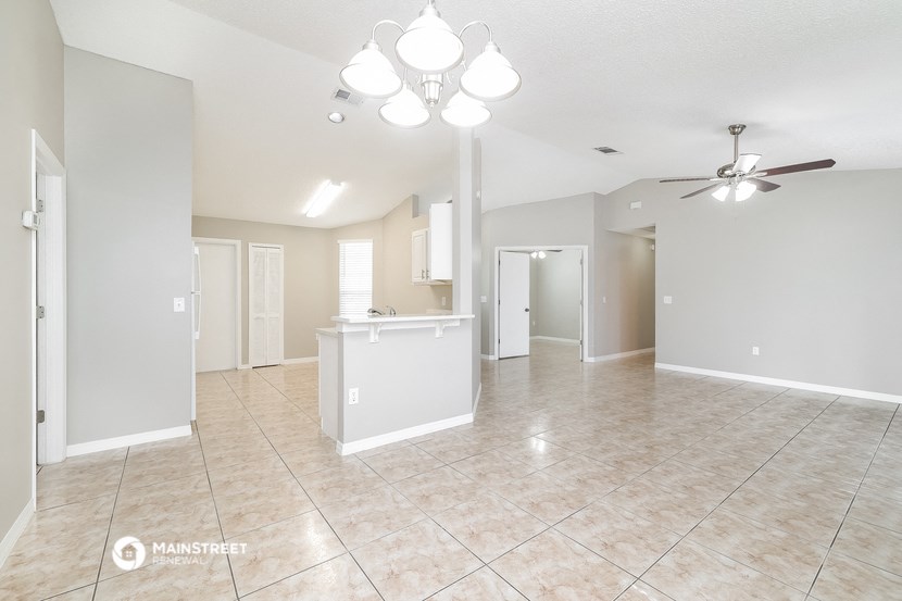 an empty living room with a kitchen and a ceiling fan