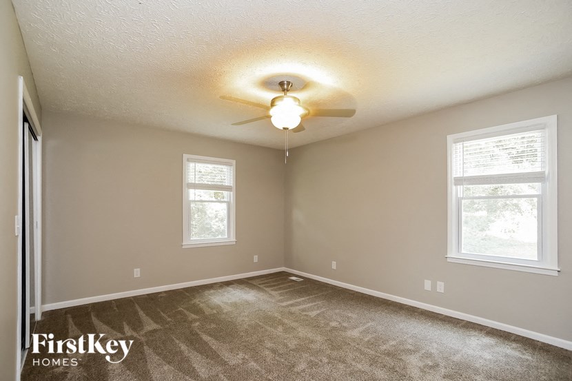 the spacious bedroom with carpeted flooring and a ceiling fan