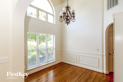 A chandelier hangs over a window in a white room.