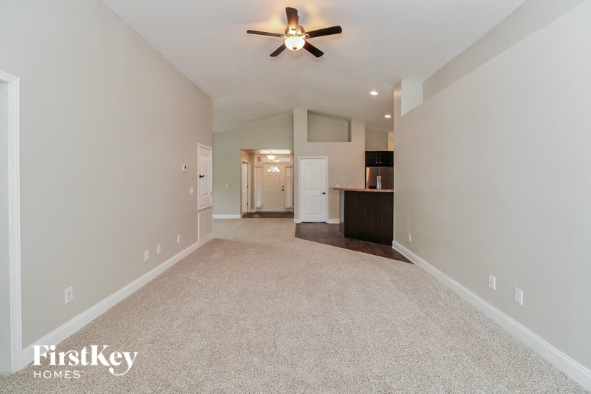an empty living room with a ceiling fan and a kitchen