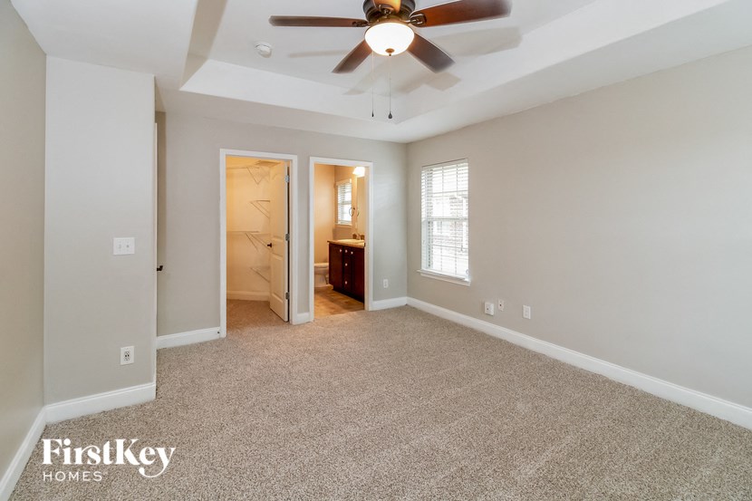 an empty living room with a ceiling fan and a door to a bathroom