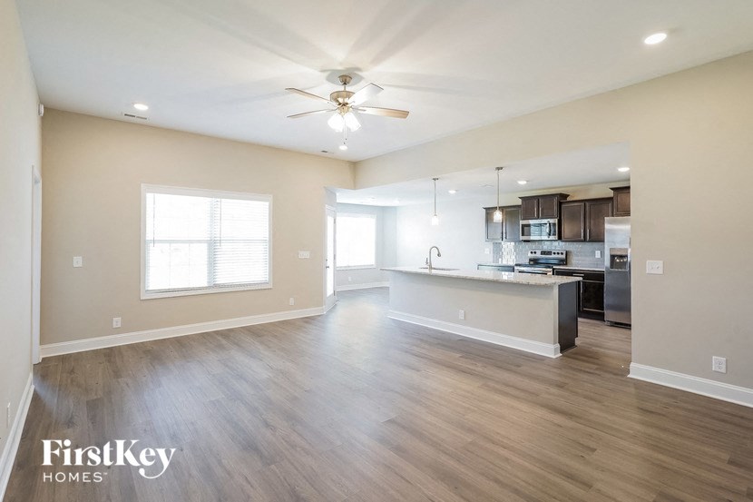 an empty living room with a kitchen and a ceiling fan
