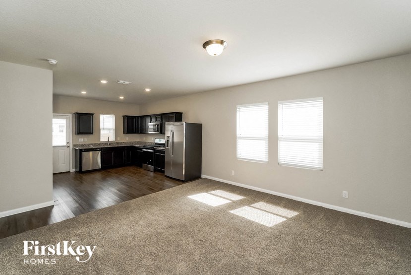an empty living room and kitchen with a stainless steel refrigerator