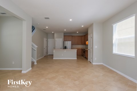 A spacious empty room with a kitchen in the background.
