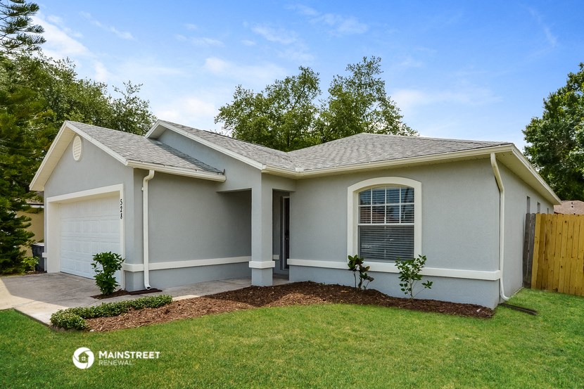 a small gray house with a lawn and a driveway