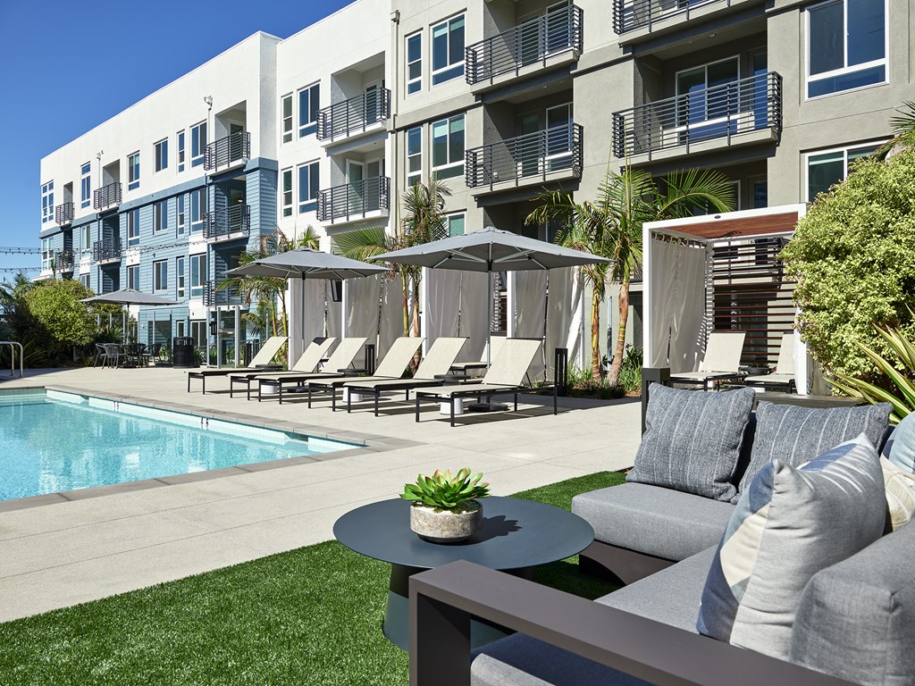 a poolside patio with chairs and a table in front of an apartment building
