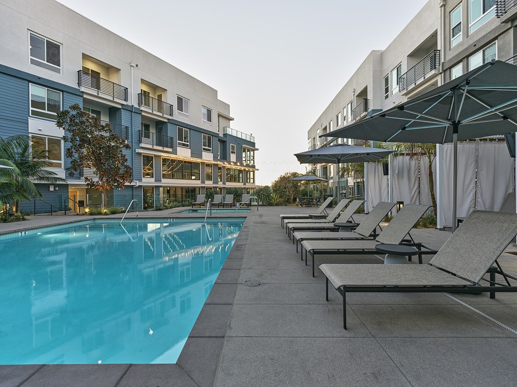 a pool with lounge chairs in front of an apartment building