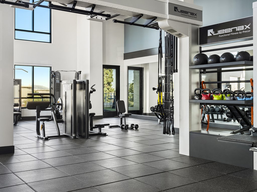 a fitness room with weights and cardio equipment and windows