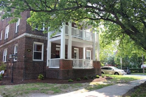 an old brick house with a porch and a tree