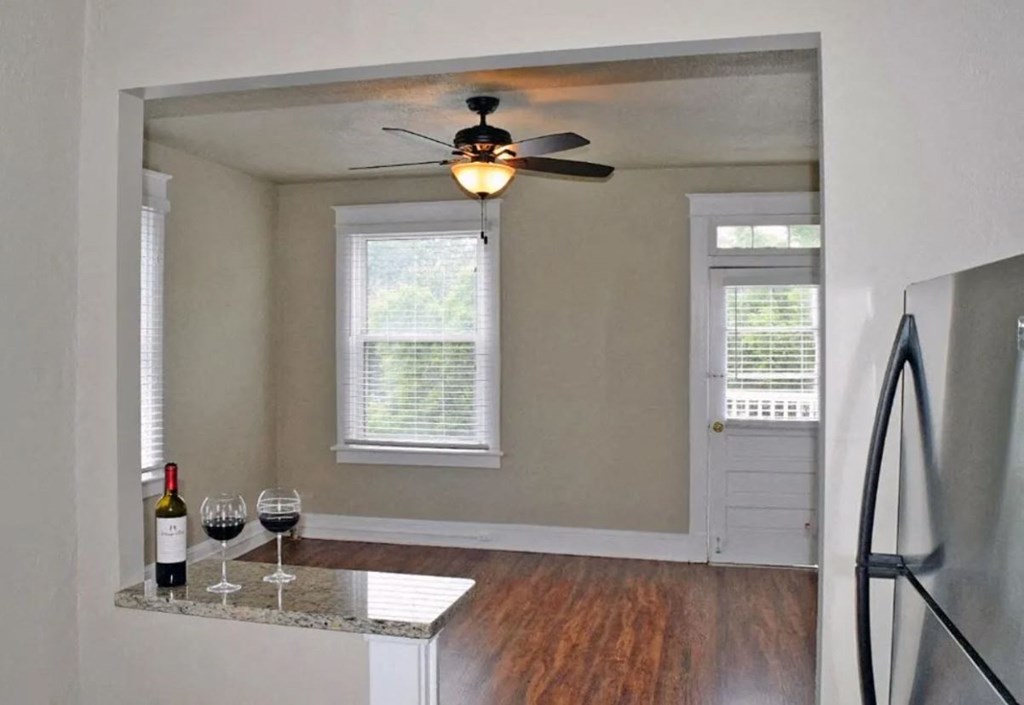 an empty living room with a ceiling fan and a table with wine glasses