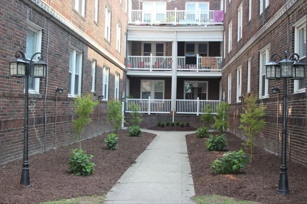 the courtyard of an apartment building with a sidewalk and plants