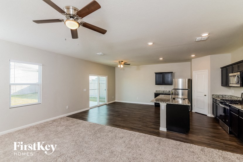 an empty living room with a kitchen and a ceiling fan