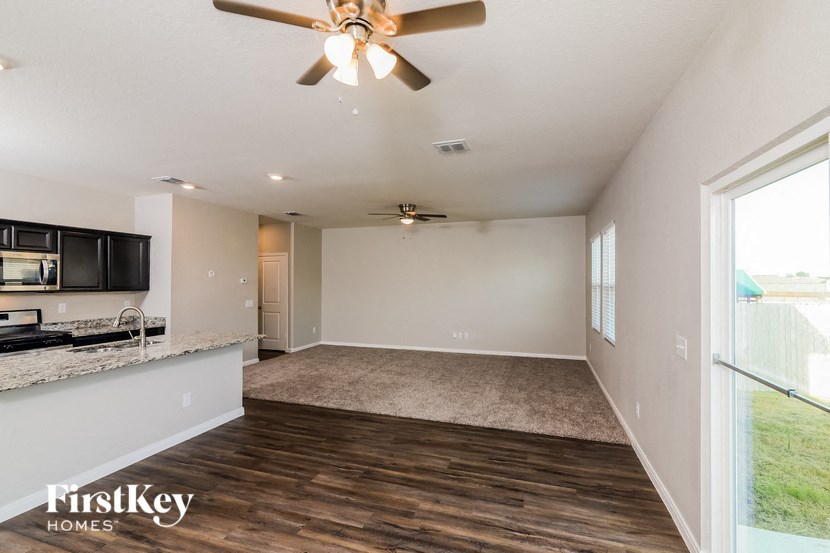 an empty living room with a kitchen and a ceiling fan
