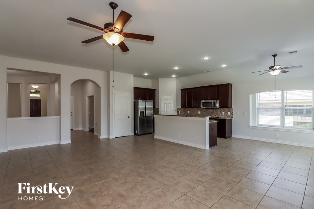 A spacious living room with a ceiling fan and a kitchen area in the background.