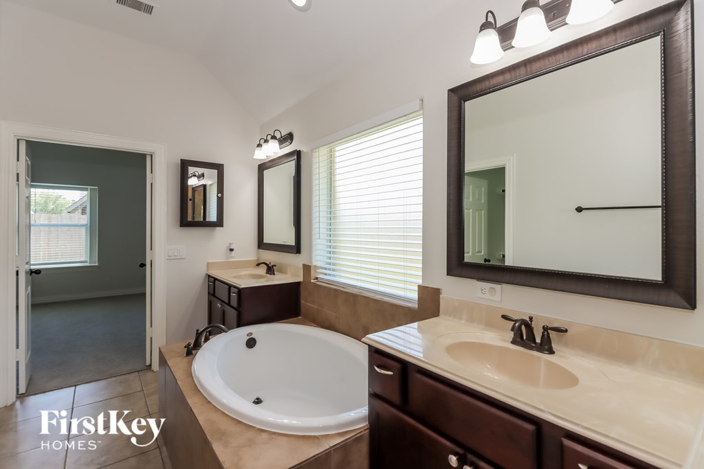 A bathroom with a tub, sink, mirror, and a window with blinds.