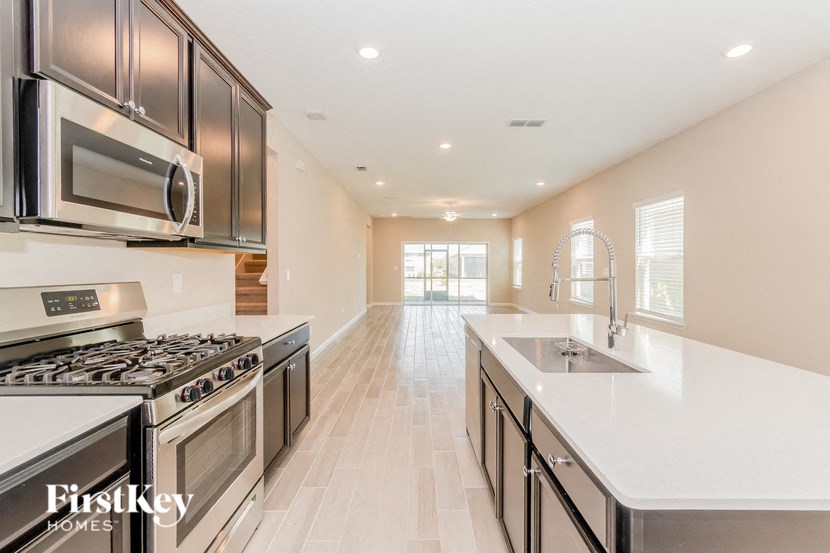 A modern kitchen with a stove, microwave, and oak flooring.
