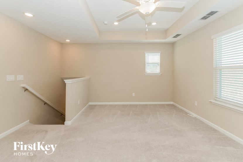 A spacious room with a staircase on the left and a window on the right.