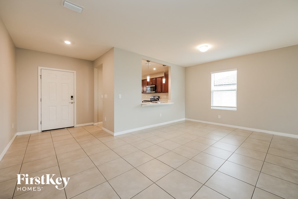 an empty living room with a white door to the kitchen