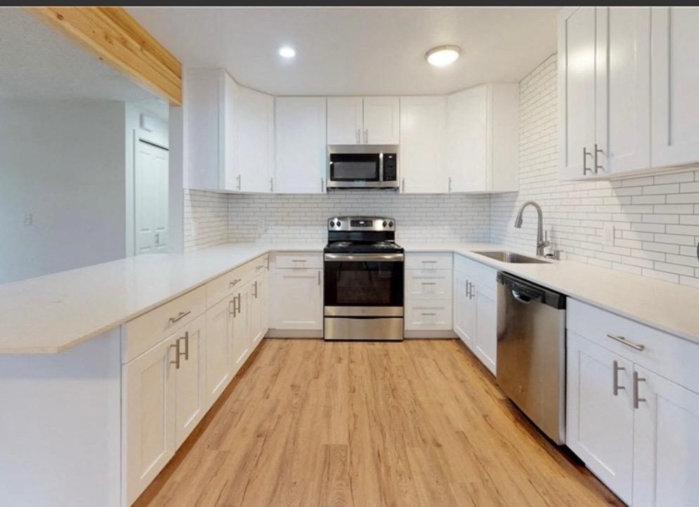 an empty kitchen with white cabinets and a wooden floor