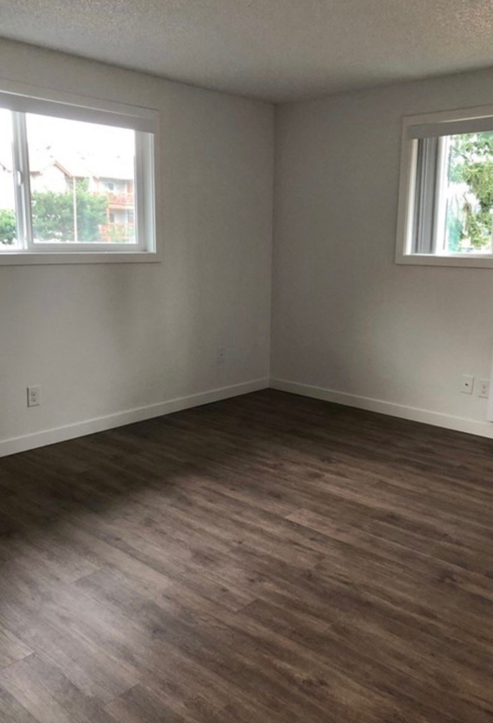 an empty living room with wooden floors and two windows