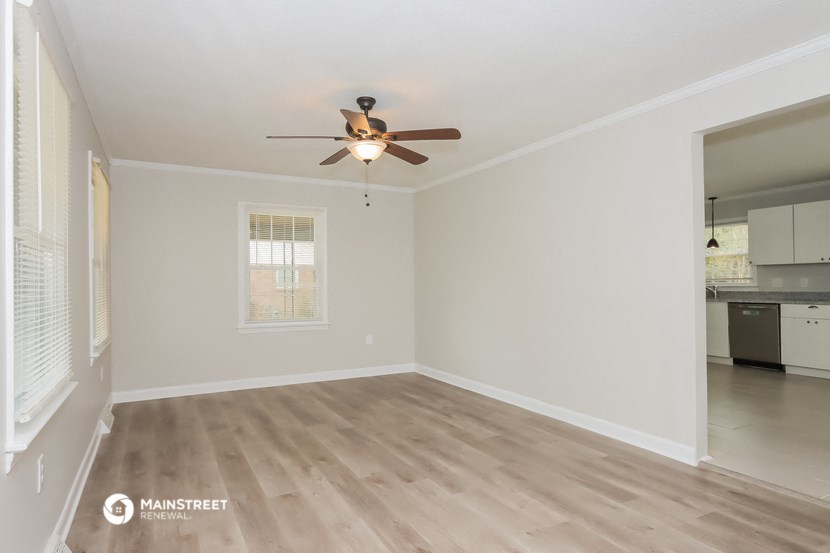 an empty living room with a ceiling fan and a kitchen
