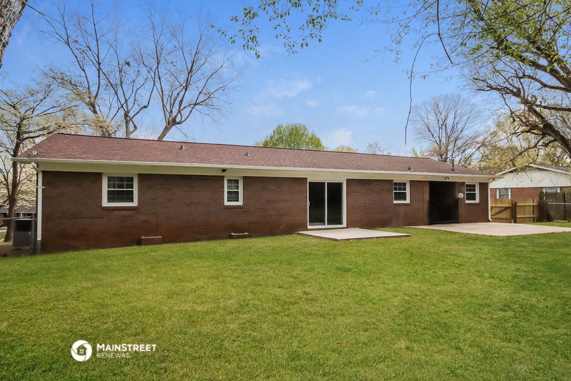 the front of a brick house with a green lawn and trees