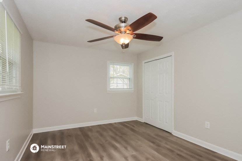 the spacious living room with ceiling fan and door to bedroom