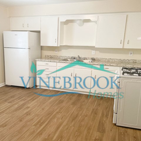 A kitchen with white appliances and cabinets with a Vinebrook Homes logo.
