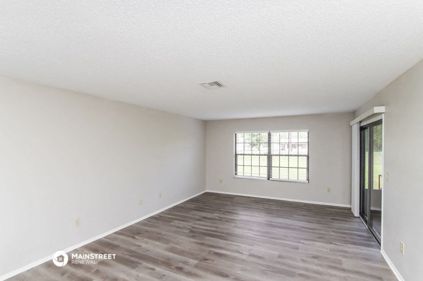 the spacious living room with white walls and wood flooring