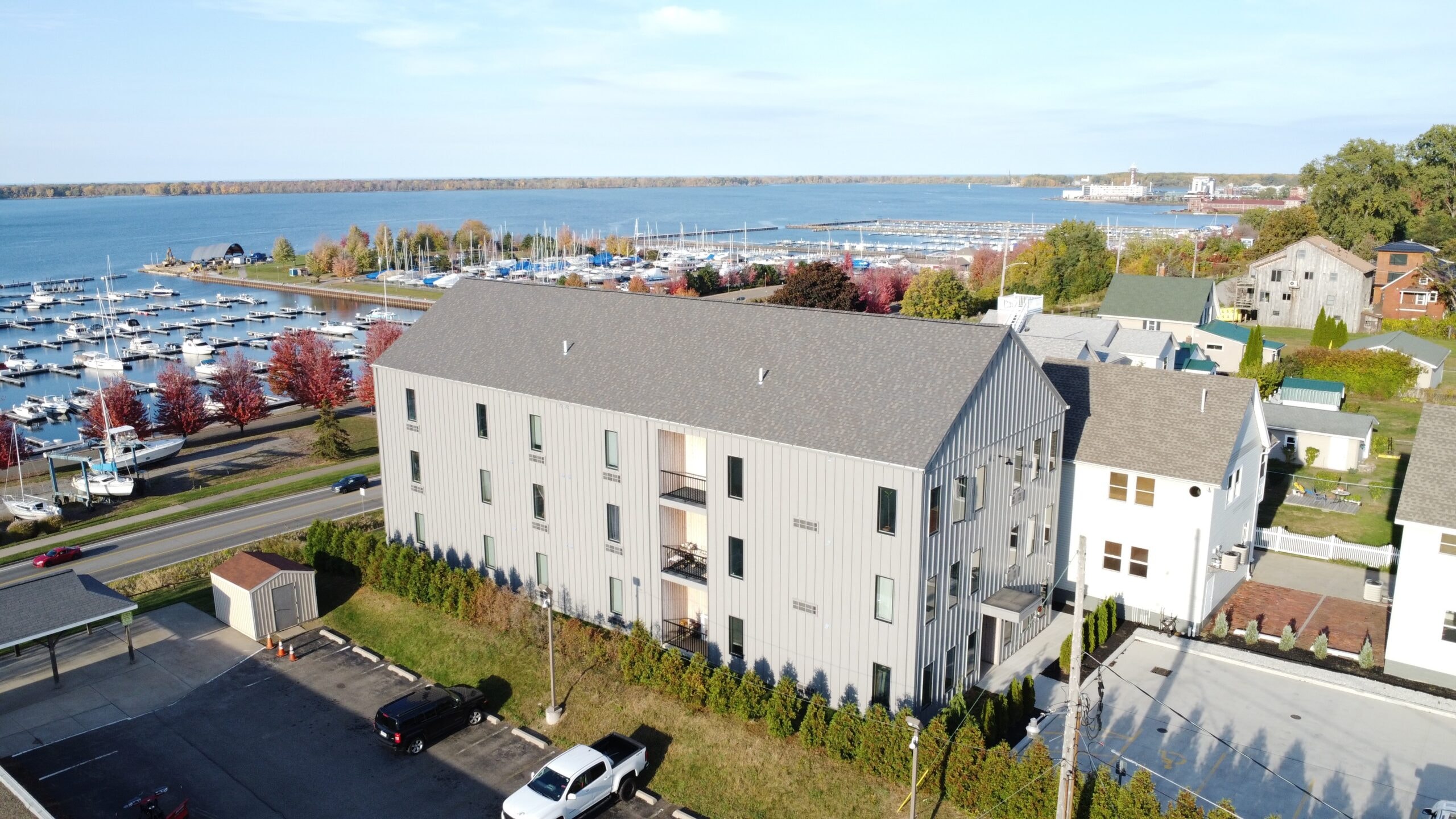 A large white building with a grey roof is surrounded by a parking lot and other buildings.