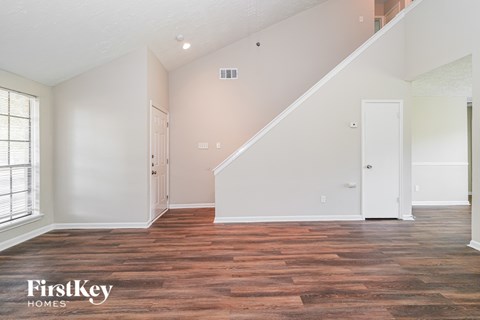 A spacious room with wooden flooring and a staircase leading to another level.
