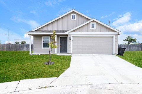 A house with a grey garage door and a small tree in front.