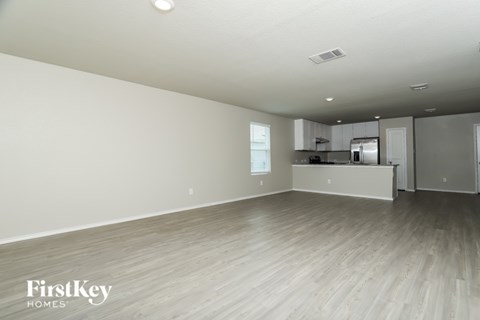 A spacious empty room with wooden flooring and a kitchen area in the background.