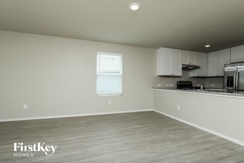 A kitchen area with wooden flooring and a window with blinds.