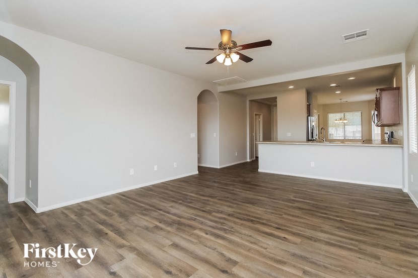 an empty living room with a ceiling fan and a kitchen
