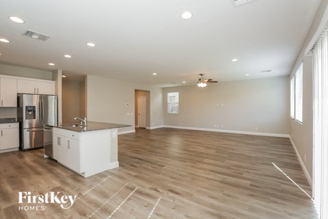 A spacious kitchen with wooden floors and a refrigerator on the left side.