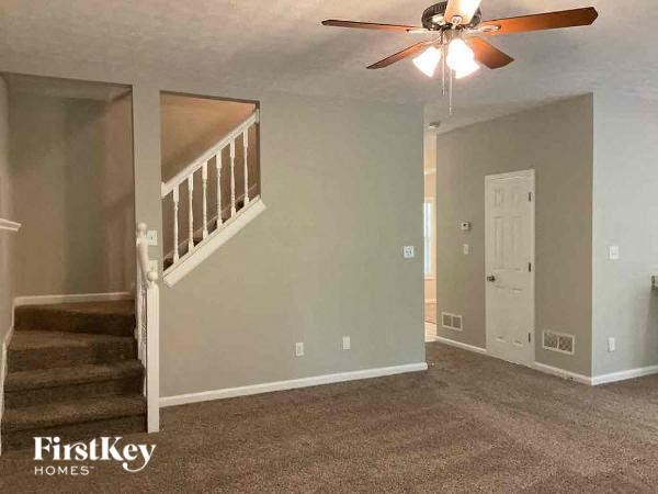 an empty living room with a ceiling fan and a staircase