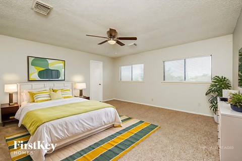 A bedroom with a bed, a ceiling fan, and a painting on the wall.