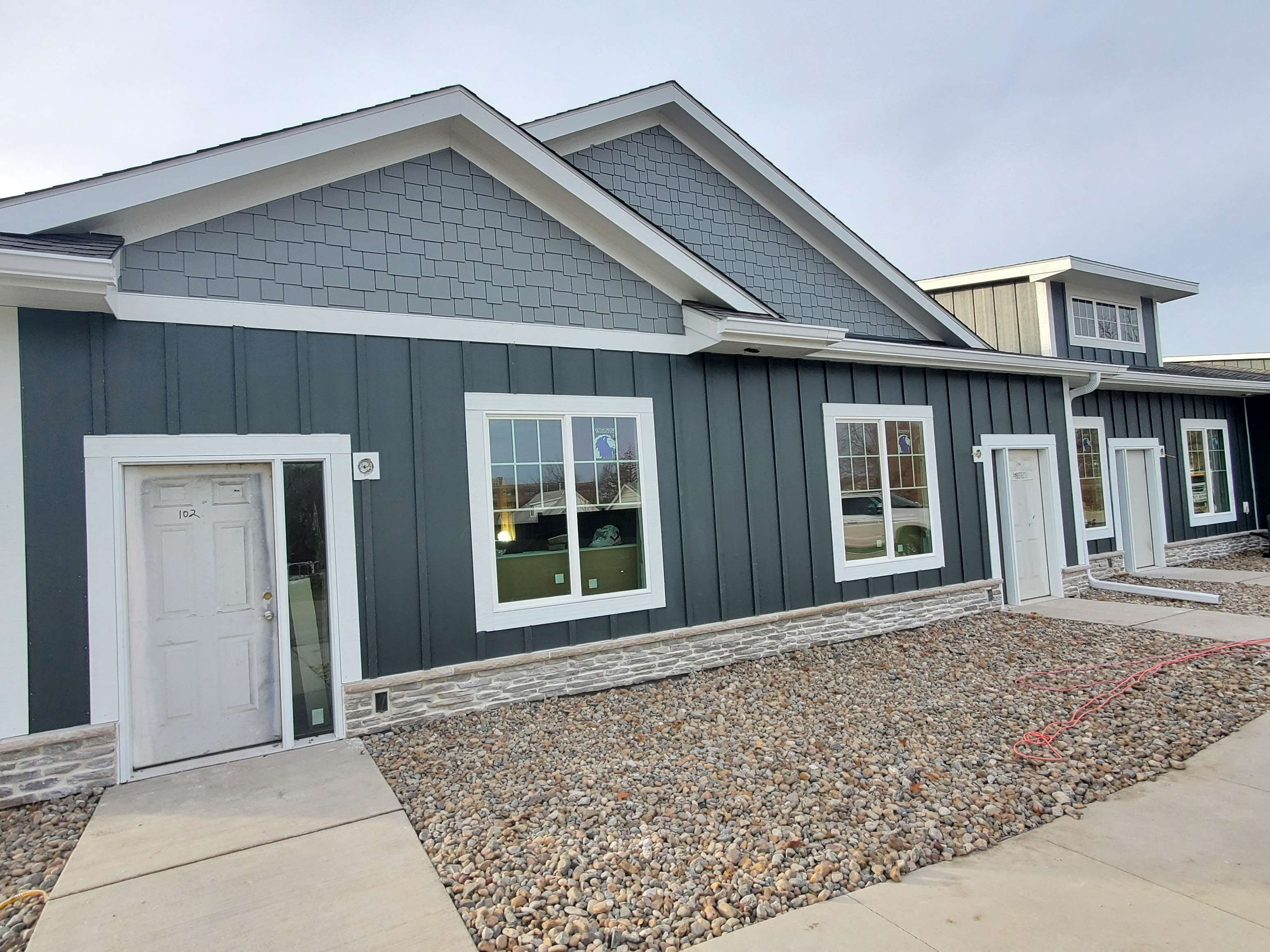 a green house with a white door and a gravel driveway