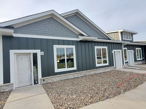 a green house with a white door and a gravel driveway