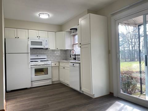 A kitchen with white appliances and cabinets with a view of trees outside.