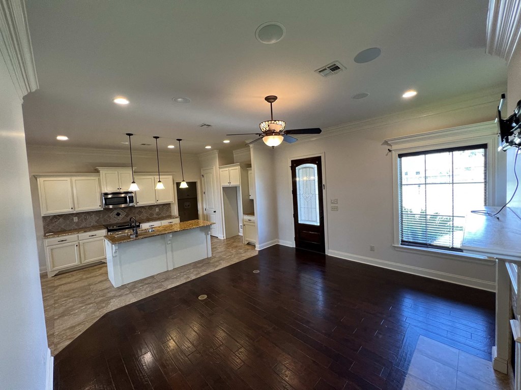 an empty living room with a kitchen and a ceiling fan