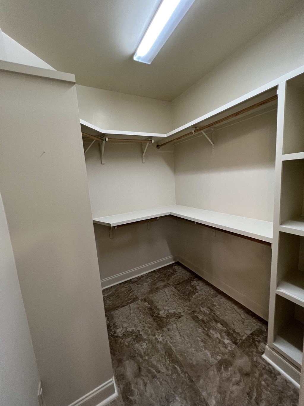 a walk in closet with white shelves and a brown floor