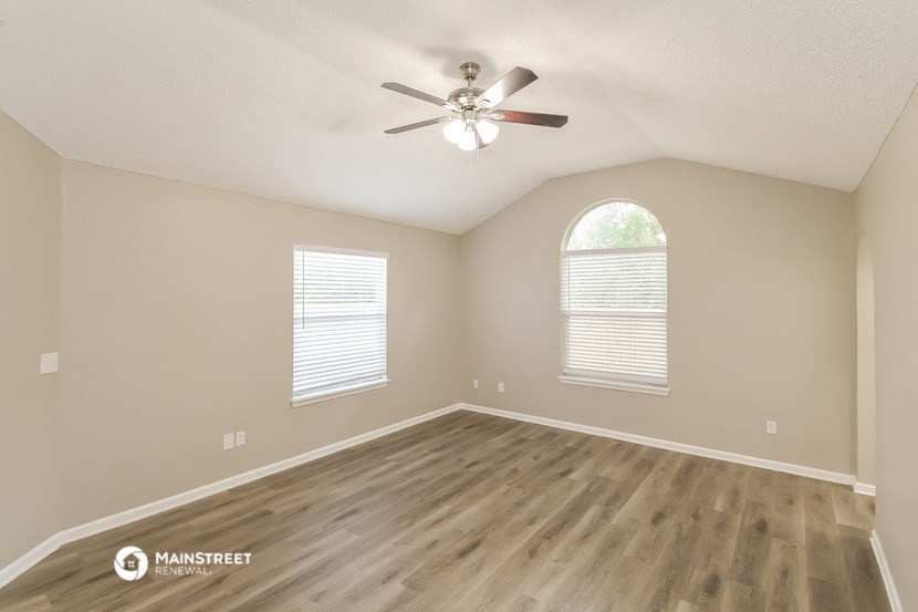 the spacious living room with hardwood flooring and a ceiling fan