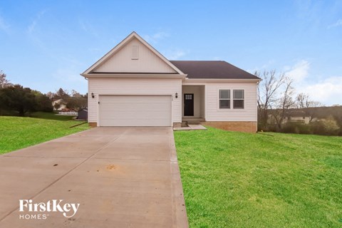 a small white house with a driveway in front of a field