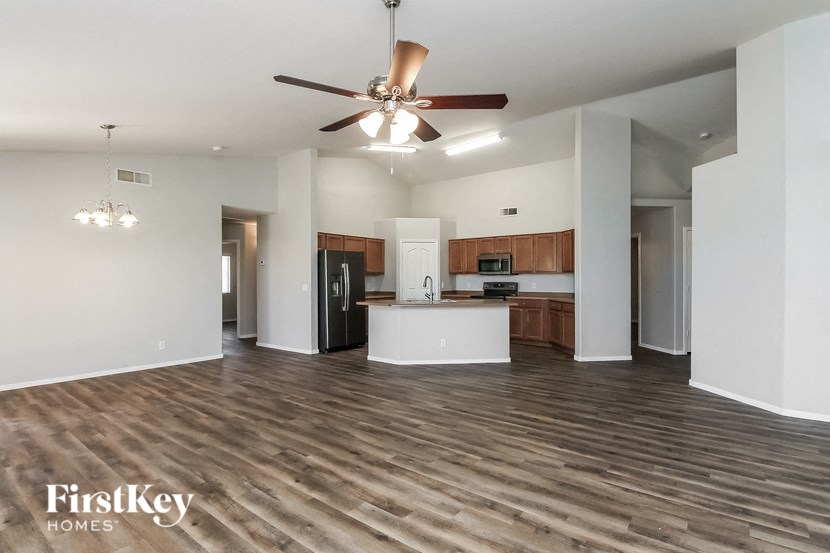 an empty living room with a ceiling fan and a kitchen