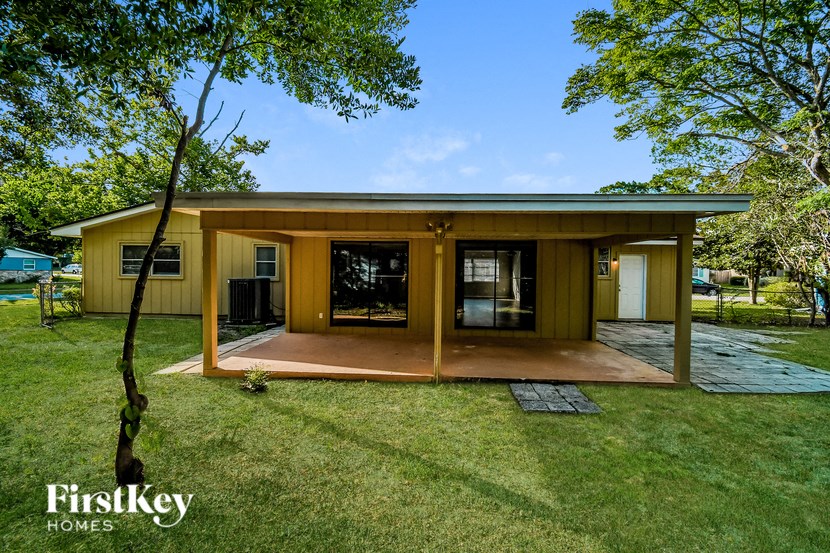 A house with a brown roof and a porch is surrounded by green grass and trees.